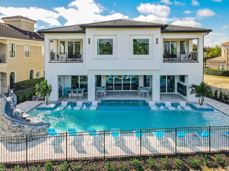 A large vacation home with a pool, lounge chairs, and waterslide.